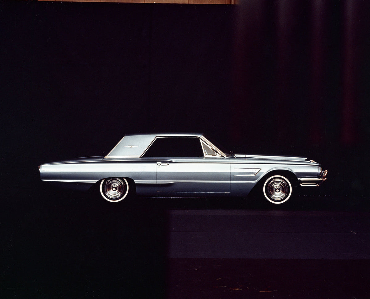 A blue 1965 Ford Thunderbird hardtop is shown in side profile against a dark studio background.