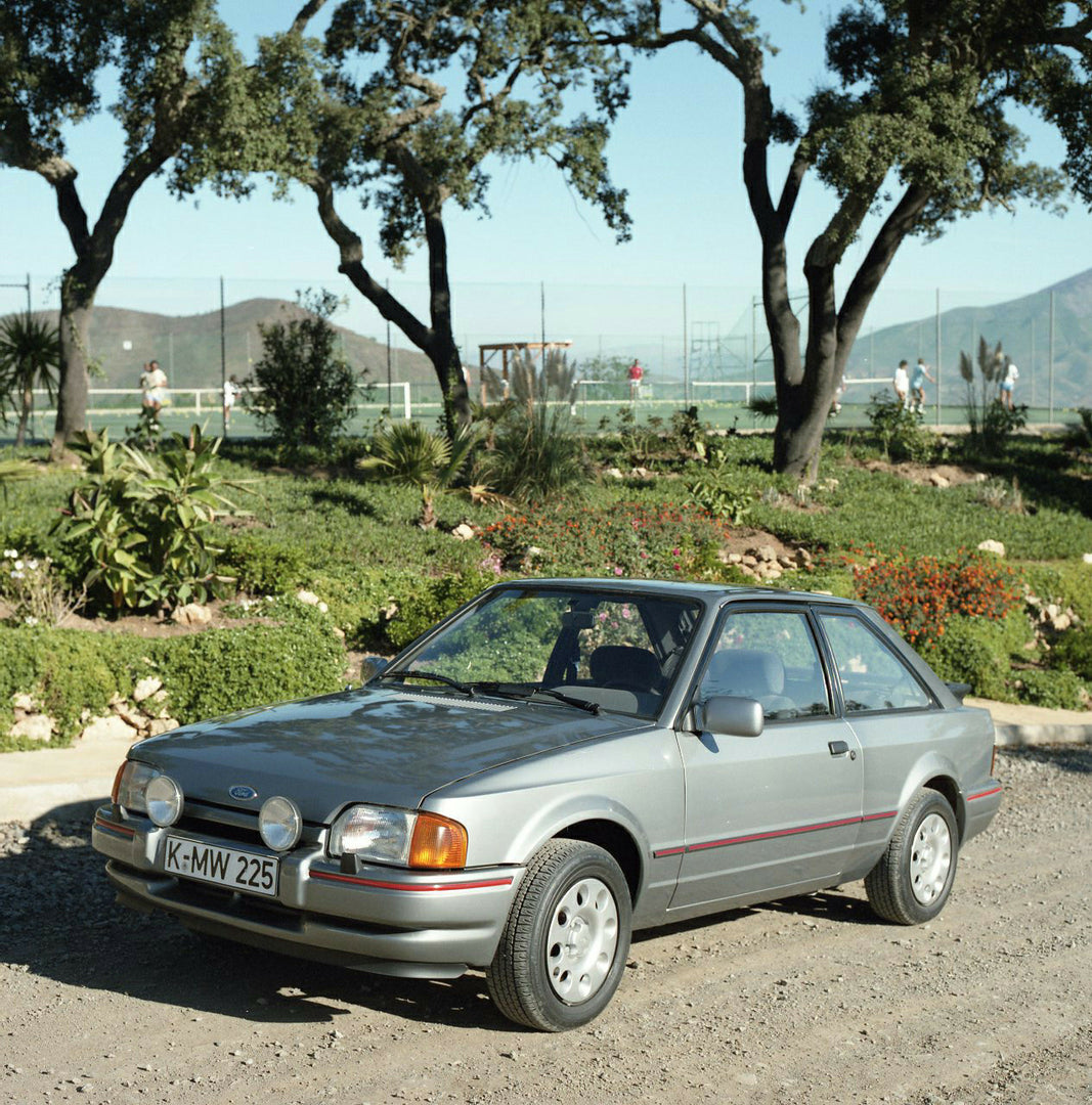 This archival image documents the 1985 Ford Escort Mark IV XR3i LHD on scenic road with trees and is preserved in the Ford Heritage Vault as part of Ford Motor Company's historic photographic archive. Free for personal, non-commercial use. Ford He...