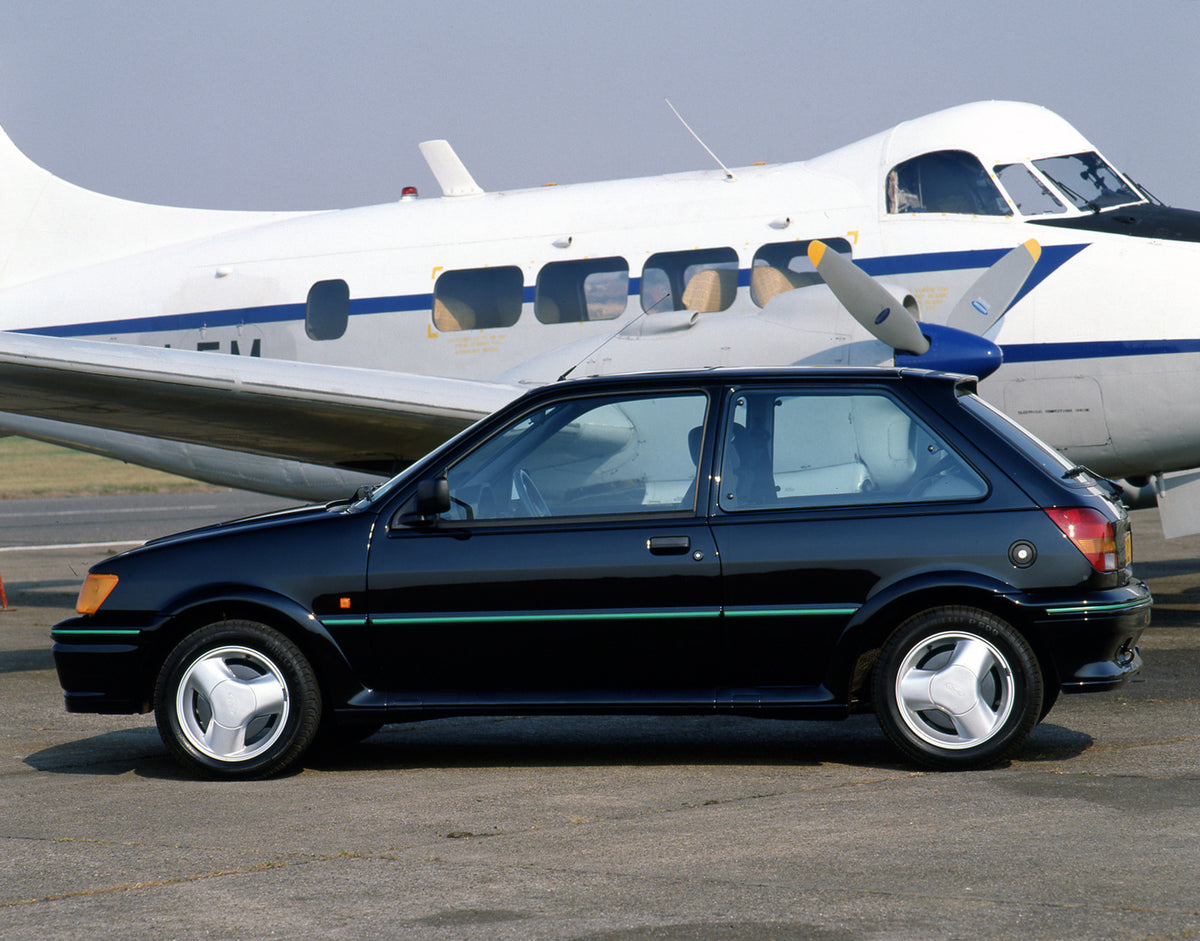 This archival image documents the 1990 Ford Fiesta Mark III Turbo side view closeup with plane and is preserved in the Ford Heritage Vault as part of Ford Motor Company's historic photographic archive. Free for personal, non-commercial use. Ford H...