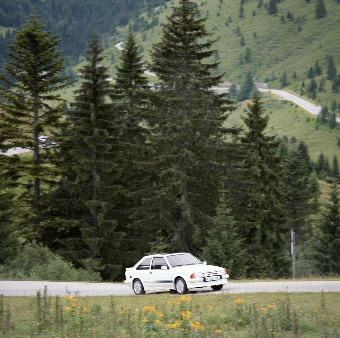 This archival image documents the 1984 Ford Escort Mark III LHD RS Turbo on scenic road with large trees in Munich and is preserved in the Ford Heritage Vault as part of Ford Motor Company's historic photographic archive. Free for personal, non-co...