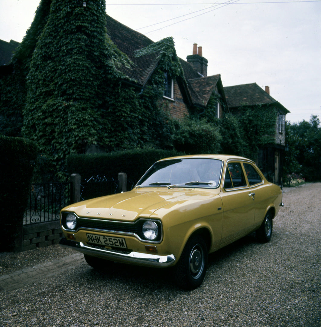 This archival image documents the 1974 Ford Escort Mark II 1100 on scenic street with ivy-covered house 1973-1009 and is preserved in the Ford Heritage Vault as part of Ford Motor Company's historic photographic archive. Free for personal, non-com...