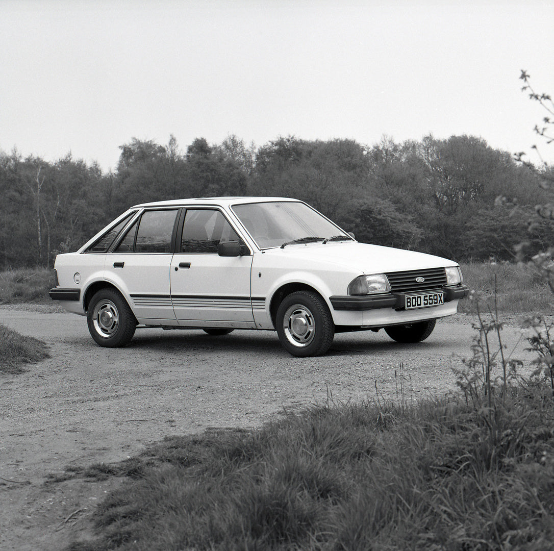 This archival image documents the 1982 Ford Escort Mark III Ghia 1.6 on scenic road with trees and is preserved in the Ford Heritage Vault as part of Ford Motor Company's historic photographic archive. Free for personal, non-commercial use. Ford H...