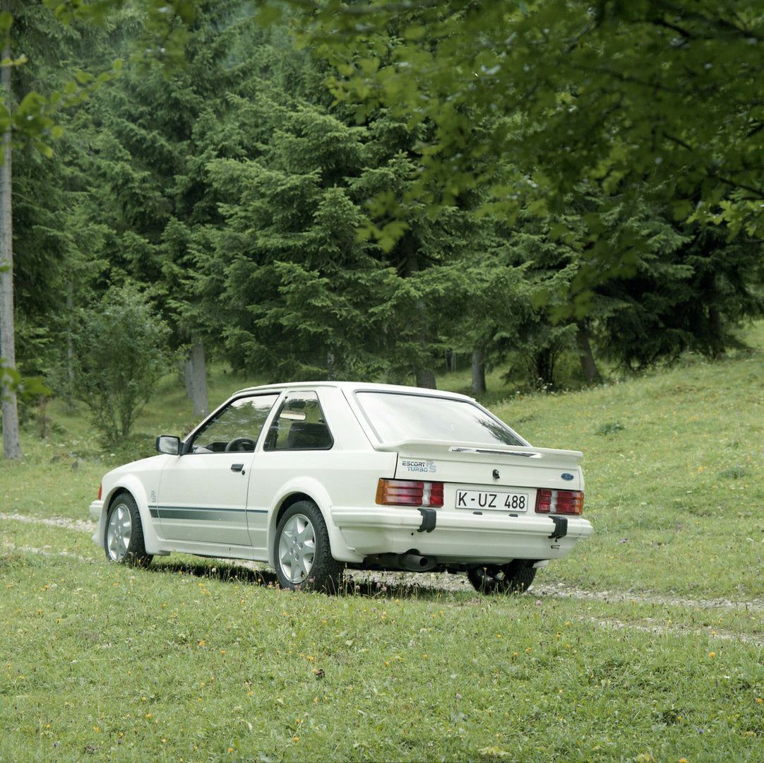 This archival image documents the 1984 Ford Escort Mark III LHD RS Turbo rear view on scenic forest road in Munich and is preserved in the Ford Heritage Vault as part of Ford Motor Company's historic photographic archive. Free for personal, non-co...