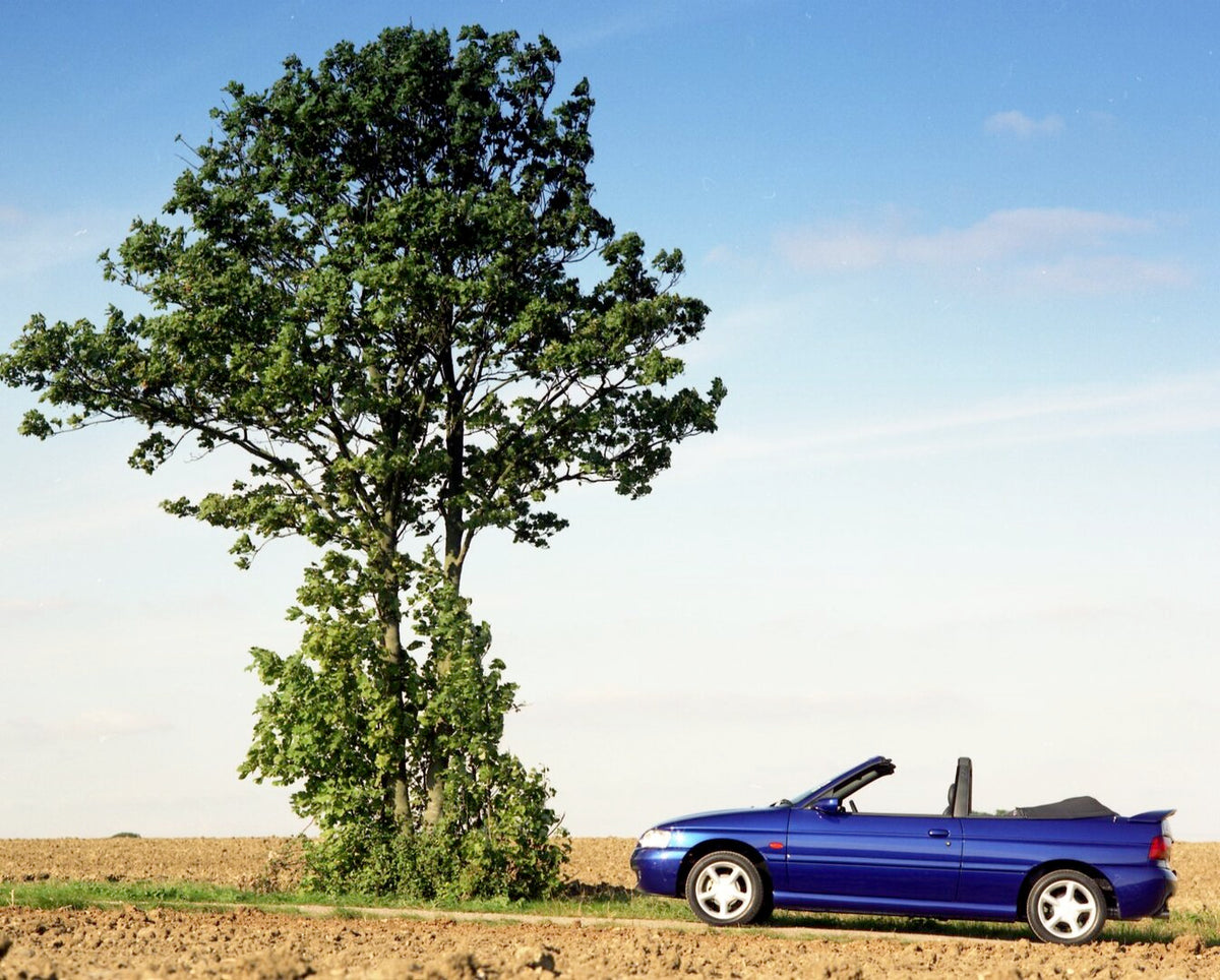 This archival image documents the 1996 Ford Escort Mark VI Cabriolet Ghia side view on scenic road with tree and is preserved in the Ford Heritage Vault as part of Ford Motor Company's historic photographic archive. Free for personal, non-commerci...