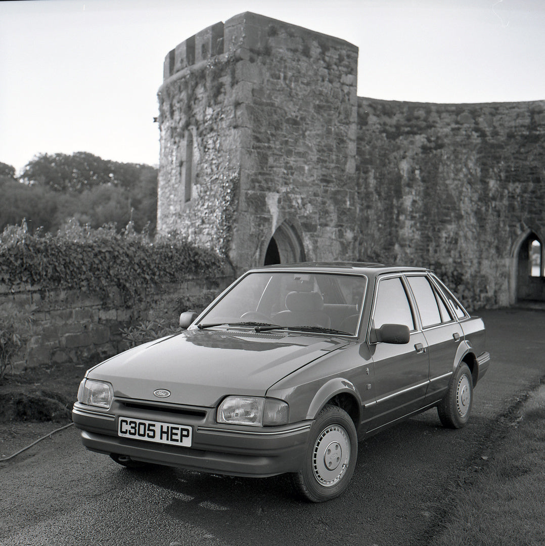 This archival image documents the 1986 Ford Escort Mark IV Ghia on scenic road with castle and is preserved in the Ford Heritage Vault as part of Ford Motor Company's historic photographic archive. Free for personal, non-commercial use. Ford Herit...