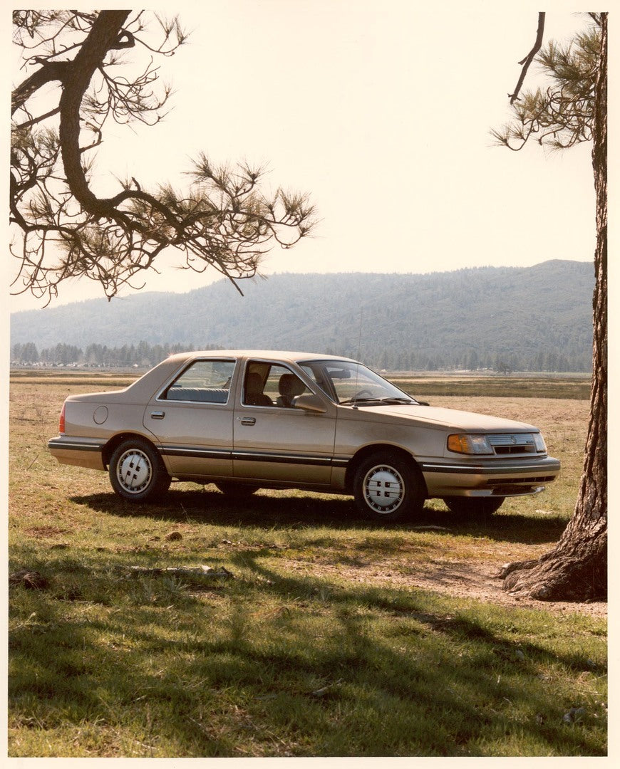 This archival image documents the 1986 Mercury Topaz with trees and mountain in background and is preserved in the Ford Heritage Vault as part of Ford Motor Company's historic photographic archive. Free for personal, non-commercial use. Ford Herit...