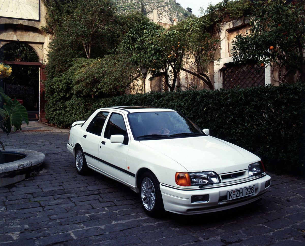 This archival image documents the 1987 Ford Sierra Cosworth LHD on scenic brick road with hedges and is preserved in the Ford Heritage Vault as part of Ford Motor Company's historic photographic archive. Free for personal, non-commercial use. Ford...