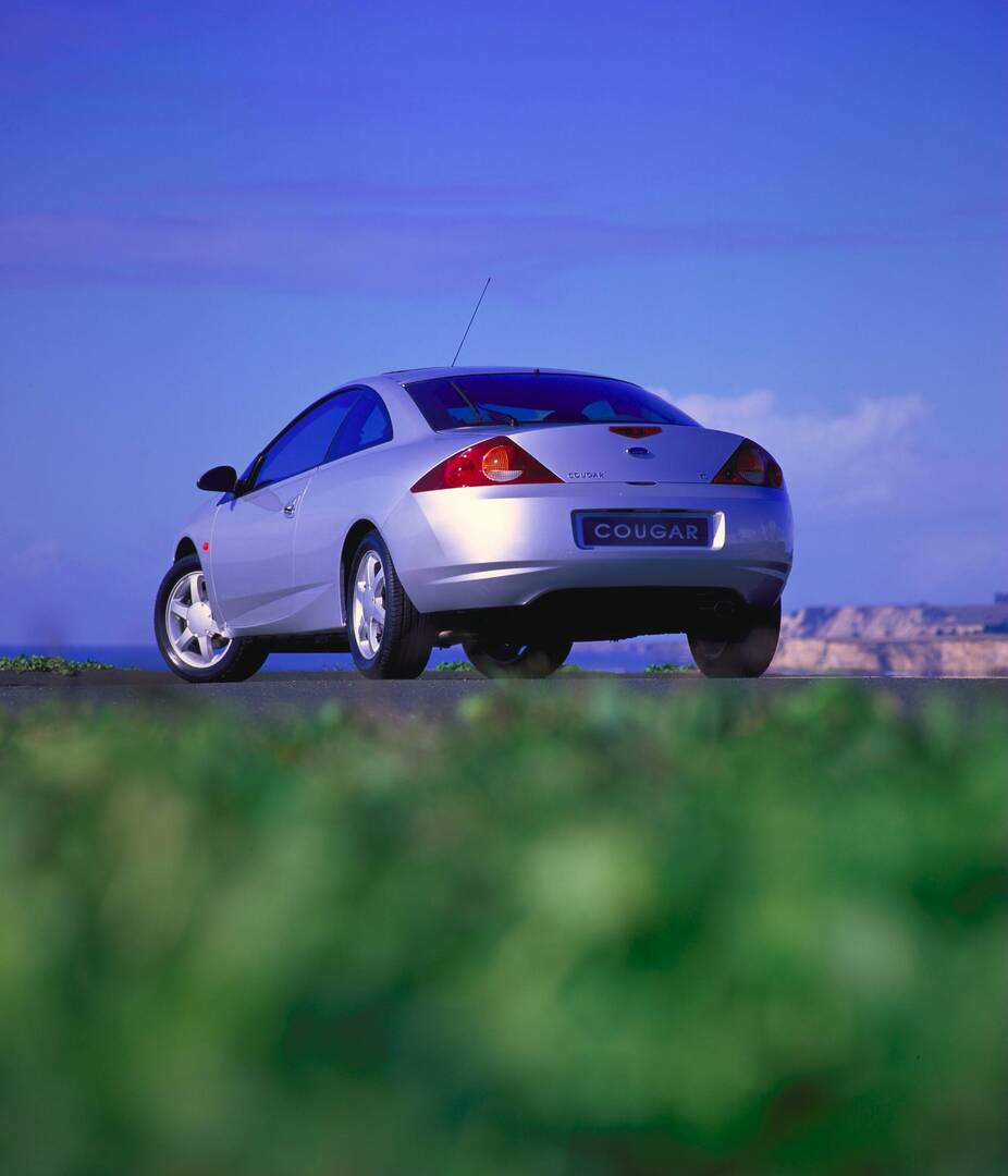 This archival image documents the 1998 Ford Cougar low view on scenic road AR-2002-213709 and is preserved in the Ford Heritage Vault as part of Ford Motor Company's historic photographic archive. Free for personal, non-commercial use. Ford Herita...