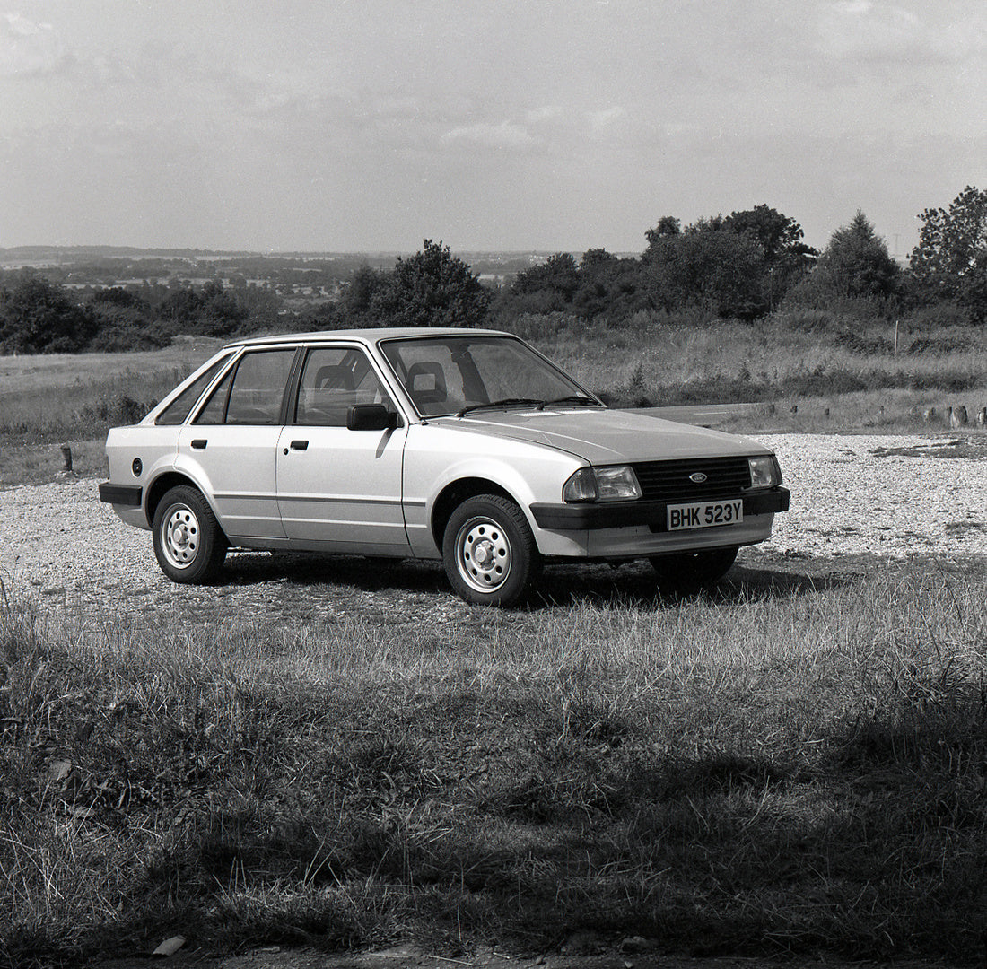 This archival image documents the 1982 Ford Escort Mark III L in gravel parking lot with scenic trees and is preserved in the Ford Heritage Vault as part of Ford Motor Company's historic photographic archive. Free for personal, non-commercial use....