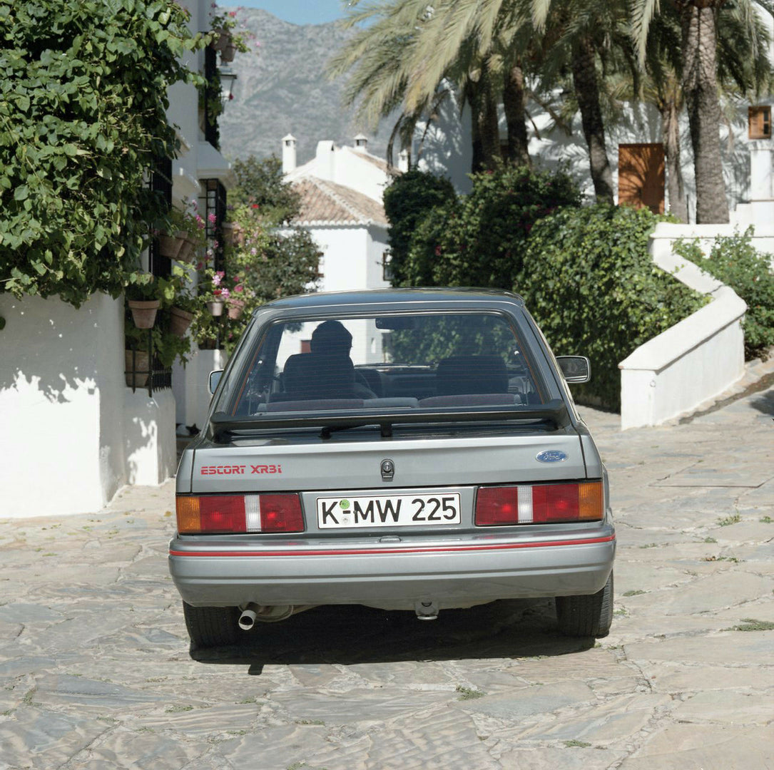 This archival image documents the 1985 Ford Escort Mark IV XR3i LHD rear view on scenic street and is preserved in the Ford Heritage Vault as part of Ford Motor Company's historic photographic archive. Free for personal, non-commercial use. Ford H...