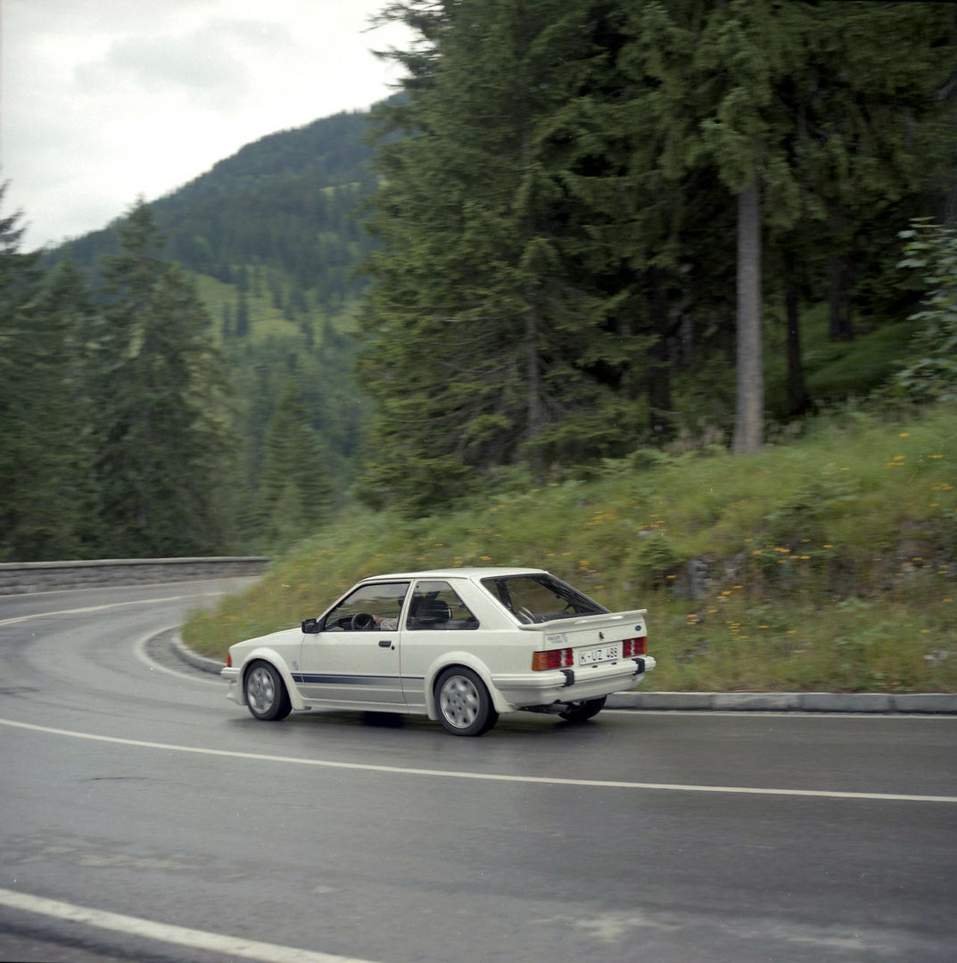 This archival image documents the 1984 Ford Escort Mark III LHD RS Turbo rear view action shot on scenic road in Munich and is preserved in the Ford Heritage Vault as part of Ford Motor Company's historic photographic archive. Free for personal, n...