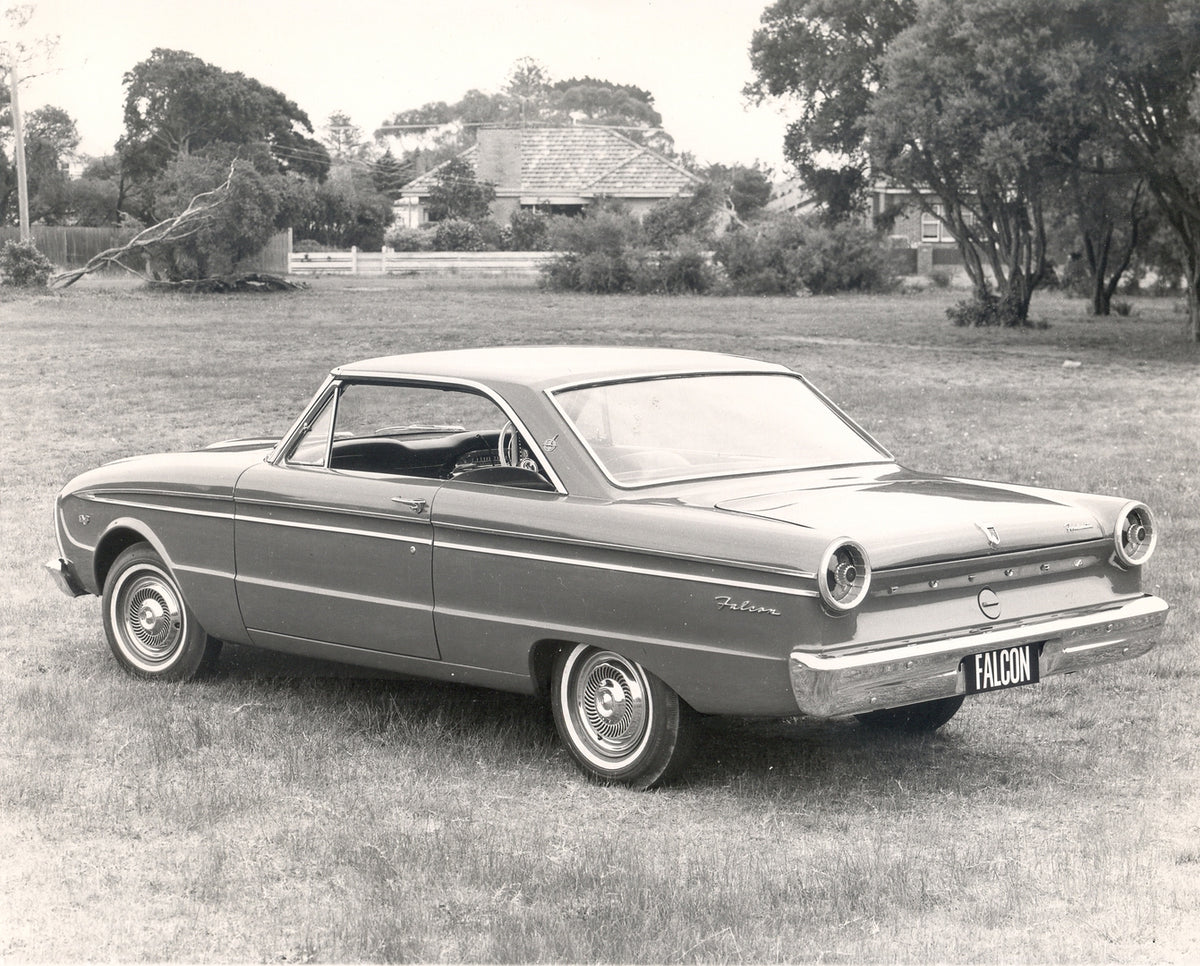 This archival image documents the 1964 Ford XM Falcon 2 Door Hardtop rear view in scenic field with houses and is preserved in the Ford Heritage Vault as part of Ford Motor Company's historic photographic archive. Free for personal, non-commercial...