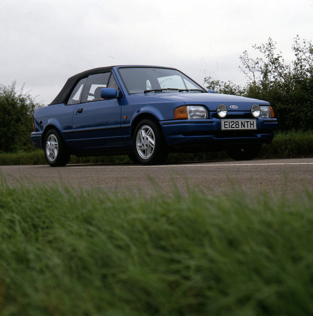 This archival image documents the 1987 Ford Escort Mark IV Cabriolet on scenic road and is preserved in the Ford Heritage Vault as part of Ford Motor Company's historic photographic archive. Free for personal, non-commercial use. Ford Heritage Vau...