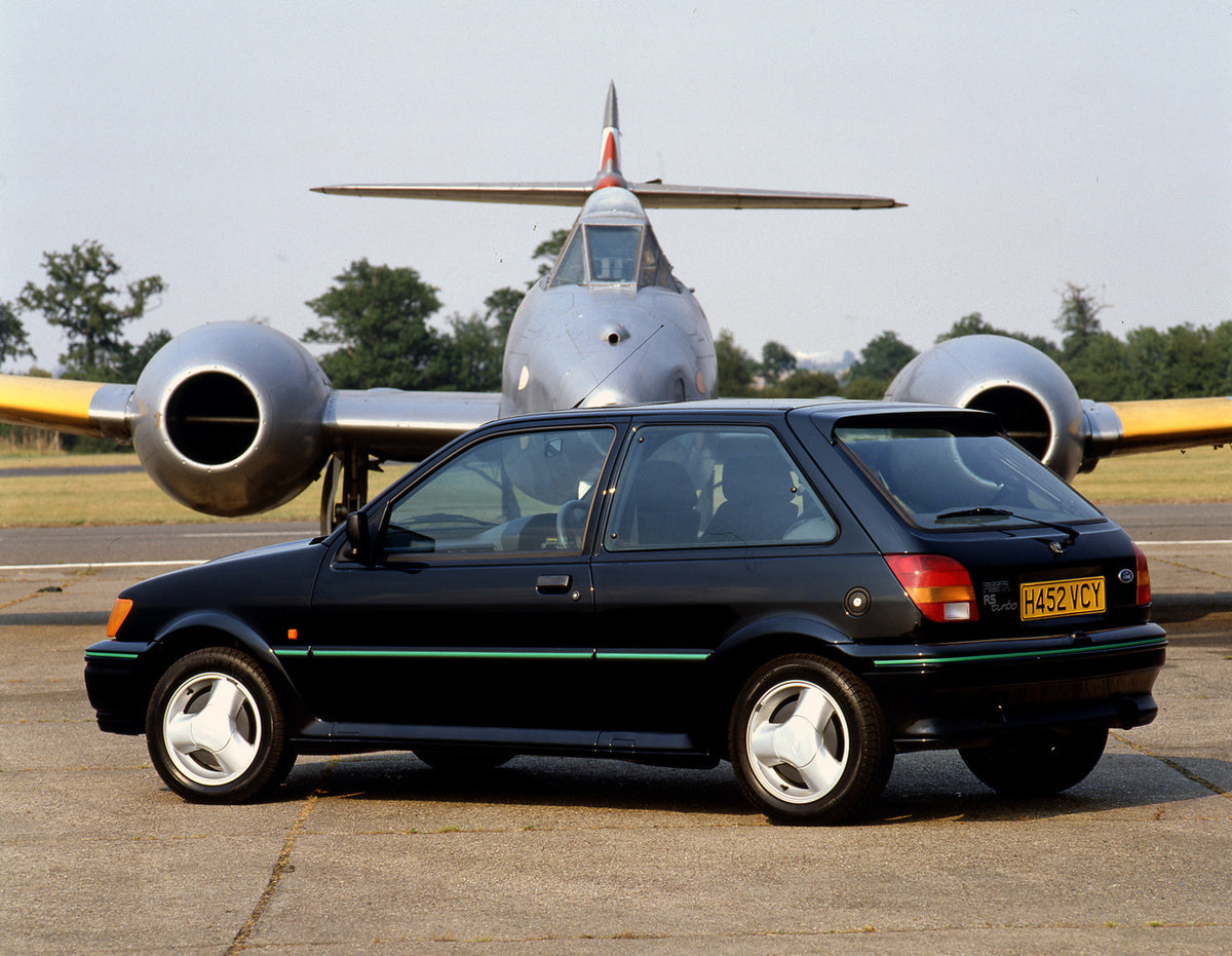 This archival image documents the 1990 Ford Fiesta Mark III Turbo rear view on tarmac with plane and is preserved in the Ford Heritage Vault as part of Ford Motor Company's historic photographic archive. Free for personal, non-commercial use. Ford...