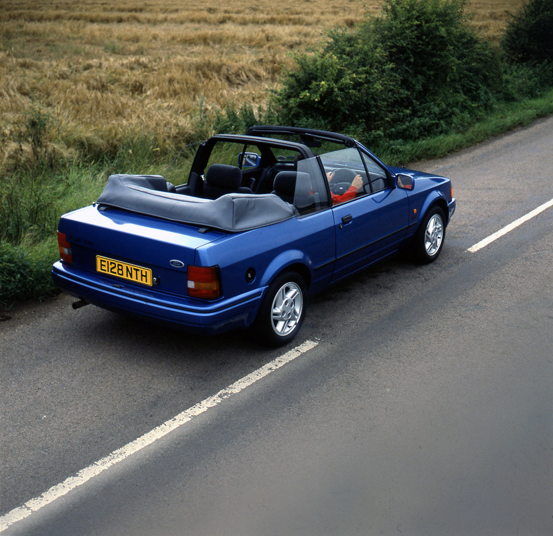 This archival image documents the 1987 Ford Escort Mark IV Cabriolet rear view on scenic road and is preserved in the Ford Heritage Vault as part of Ford Motor Company's historic photographic archive. Free for personal, non-commercial use. Ford He...