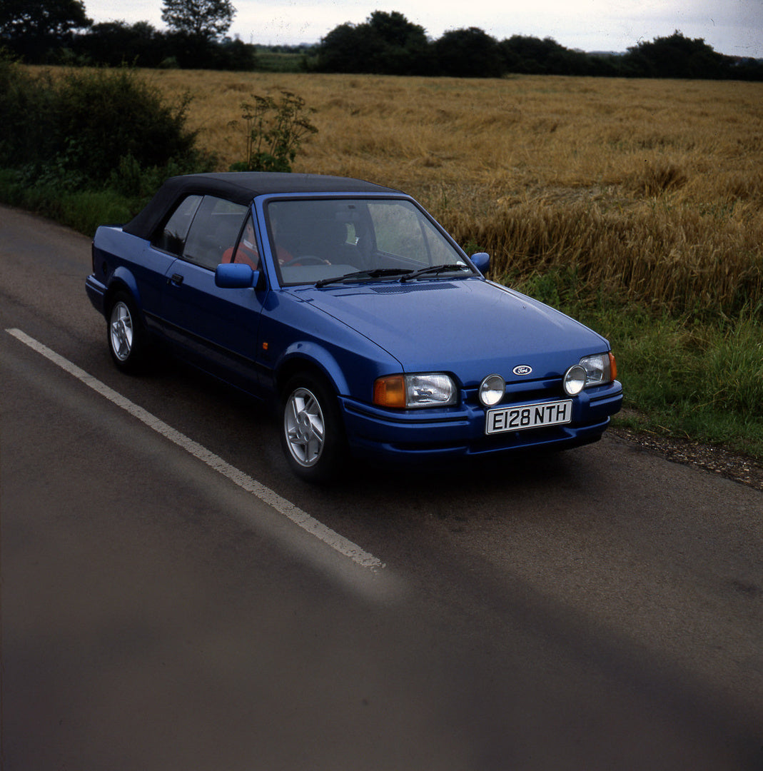 This archival image documents the 1987 Ford Escort Mark IV Cabriolet on scenic road and is preserved in the Ford Heritage Vault as part of Ford Motor Company's historic photographic archive. Free for personal, non-commercial use. Ford Heritage Vau...