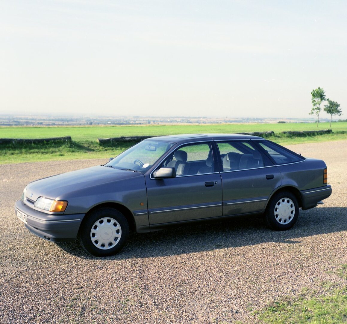 This archival image documents the 1987 Ford Granada Ghia 2.4i side view on scenic road with field and is preserved in the Ford Heritage Vault as part of Ford Motor Company's historic photographic archive. Free for personal, non-commercial use. For...