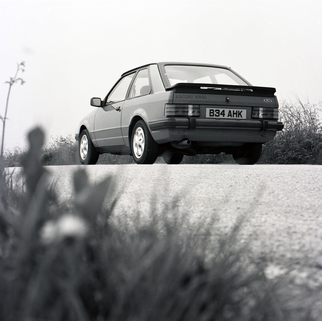 This archival image documents the 1985 Ford Escort Mark III XR3i low rear view on scenic road and is preserved in the Ford Heritage Vault as part of Ford Motor Company's historic photographic archive. Free for personal, non-commercial use. Ford He...