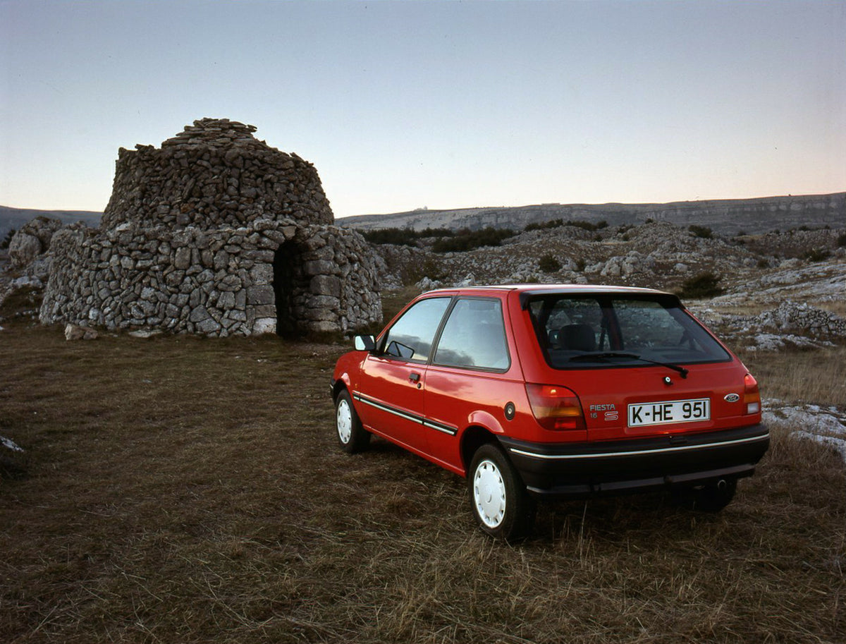 This archival image documents the 1989 Ford Fiesta Mark III LHD rear view with scenic stone structure and is preserved in the Ford Heritage Vault as part of Ford Motor Company's historic photographic archive. Free for personal, non-commercial use....