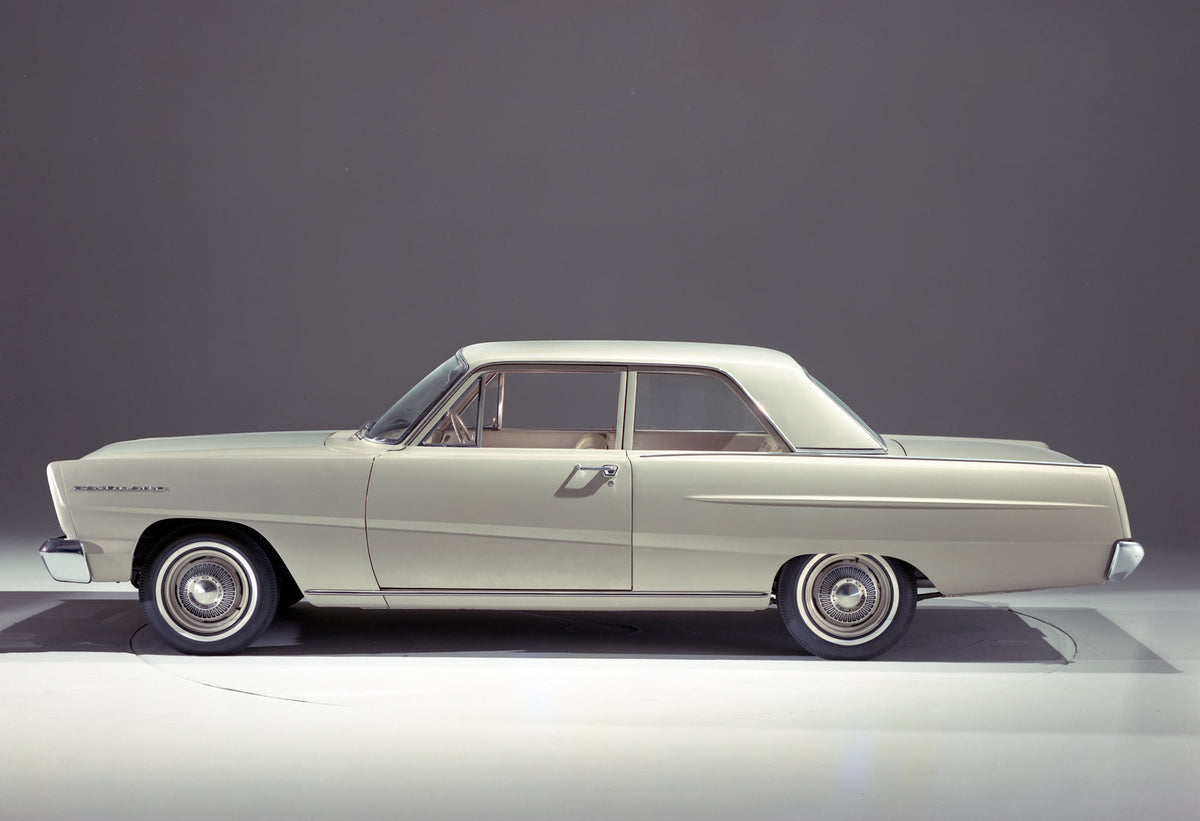 A pale 1965 Ford Fairlane two-door sedan is shown in side profile against a gray studio background, with its fixed center pillar and side trim visible.