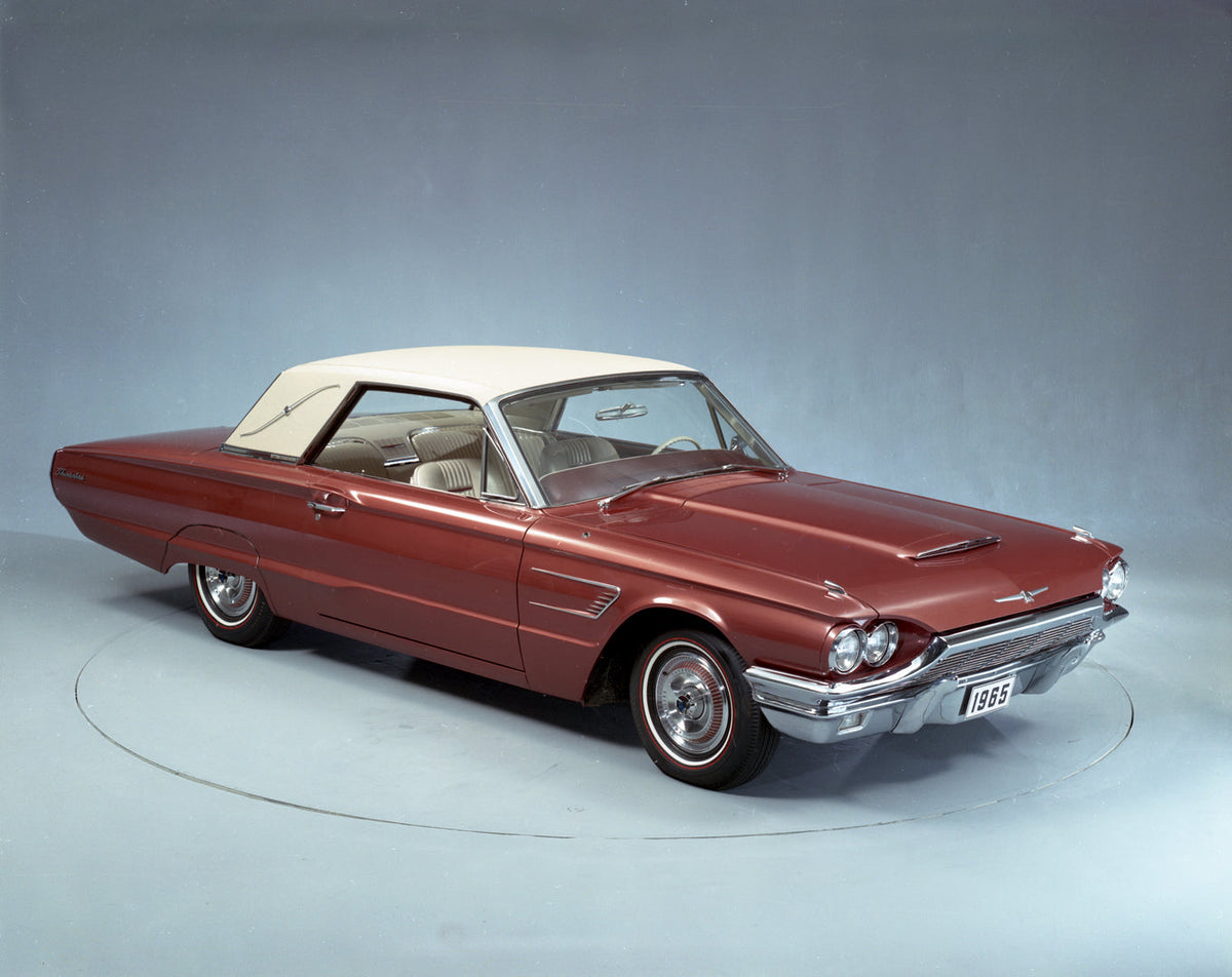 A red 1965 Ford Thunderbird Landau with a light-colored roof is photographed from the front in a studio.