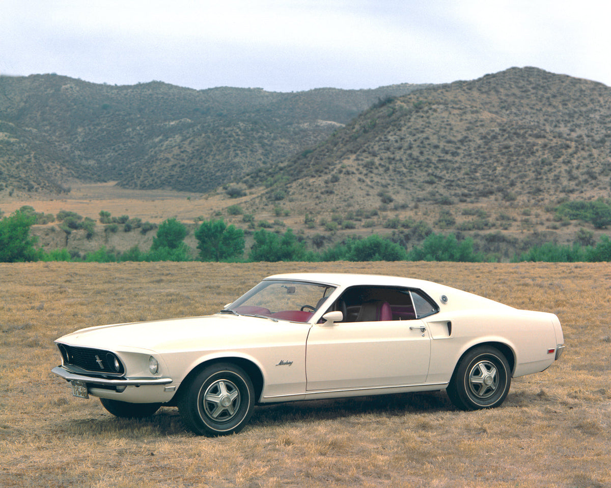 A pale yellow 1969 Ford Mustang SportsRoof is shown from the front three-quarter angle in a dry field.