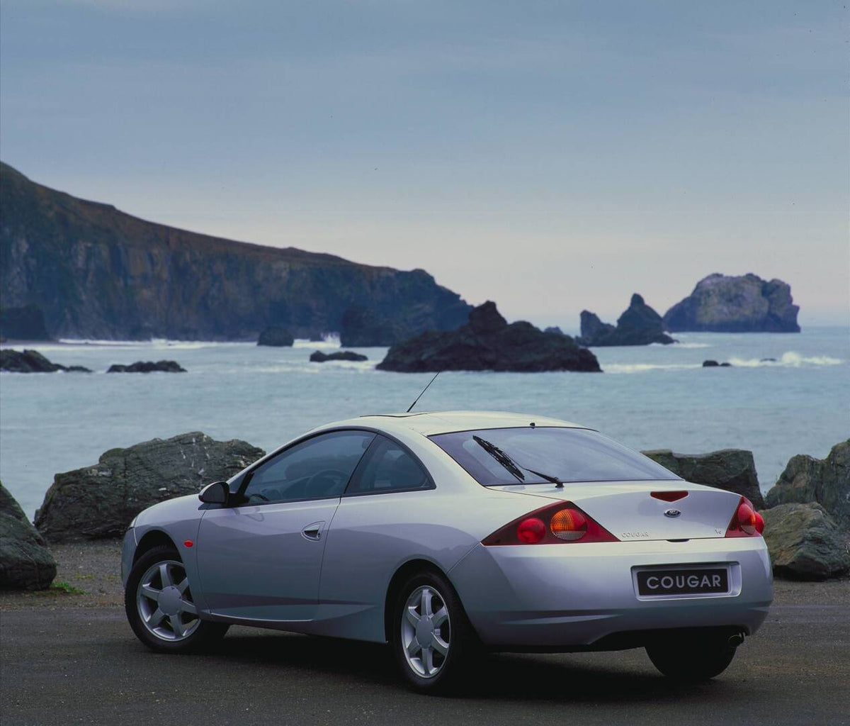 This archival image documents the 1998 Ford Cougar rear view near scenic body of water with rocky beach AR-2002-213709 and is preserved in the Ford Heritage Vault as part of Ford Motor Company's historic photographic archive. Free for personal, no...