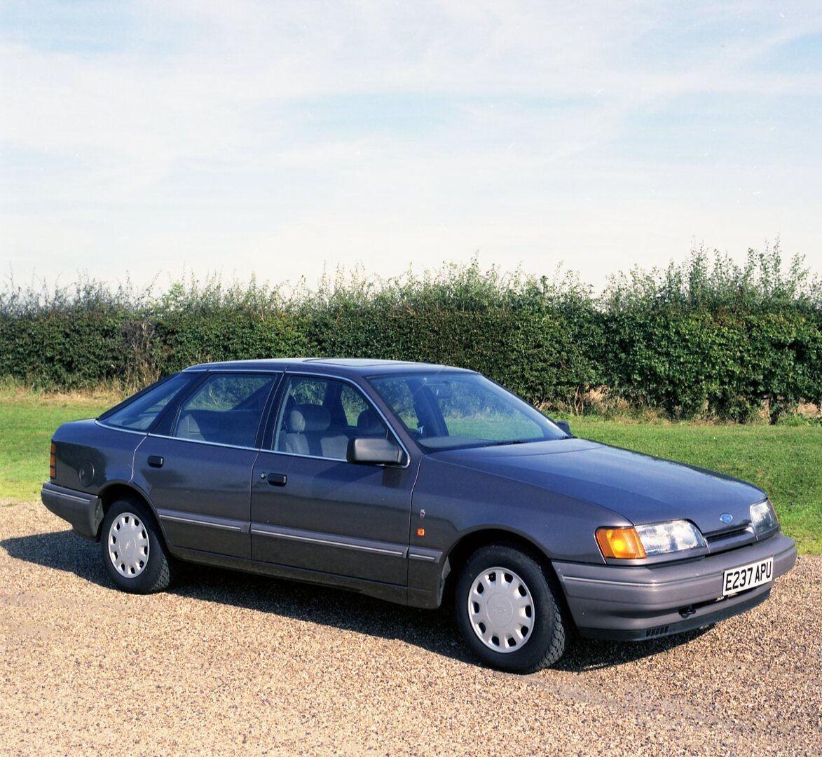 This archival image documents the 1987 Ford Granada Ghia 2.4i on scenic road with shrubs and is preserved in the Ford Heritage Vault as part of Ford Motor Company's historic photographic archive. Free for personal, non-commercial use. Ford Heritag...