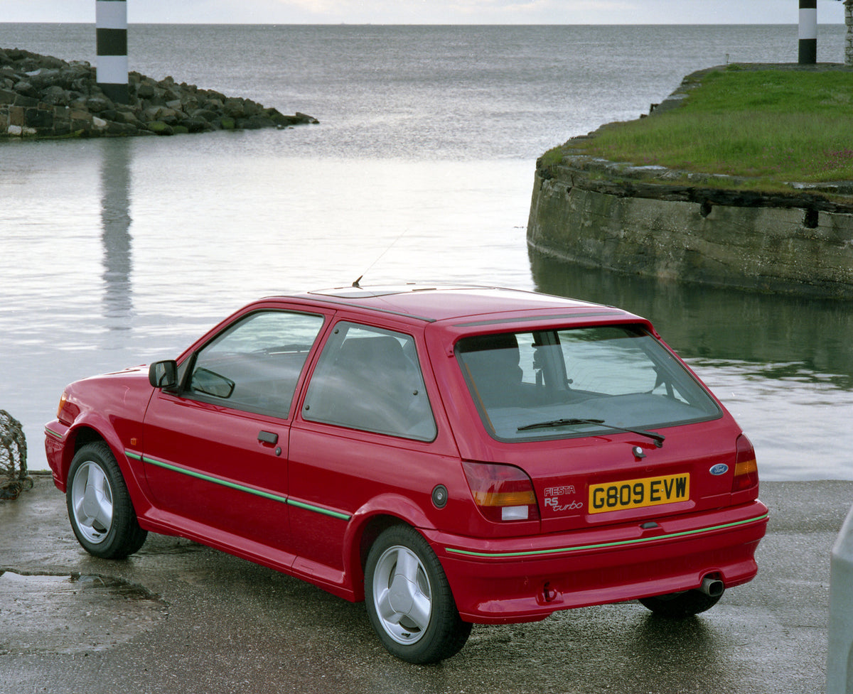 This archival image documents the 1990 Ford Fiesta Mark III Turbo rear view near scenic ocean in Northern Ireland and is preserved in the Ford Heritage Vault as part of Ford Motor Company's historic photographic archive. Free for personal, non-com...