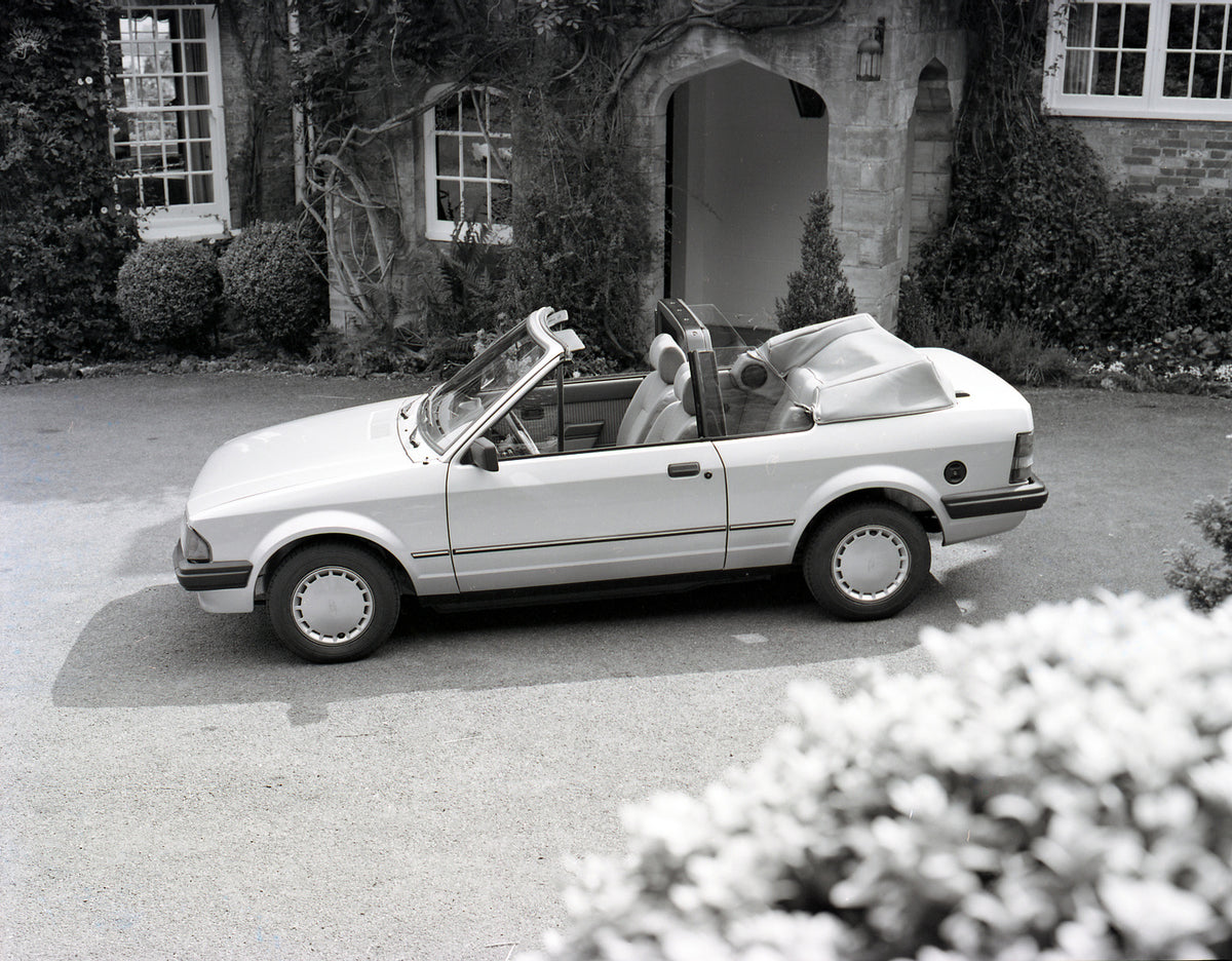 This archival image documents the 1983 Ford Escort Mark III Cabriolet 1.6i in front of scenic house with ivy and is preserved in the Ford Heritage Vault as part of Ford Motor Company's historic photographic archive. Free for personal, non-commerci...
