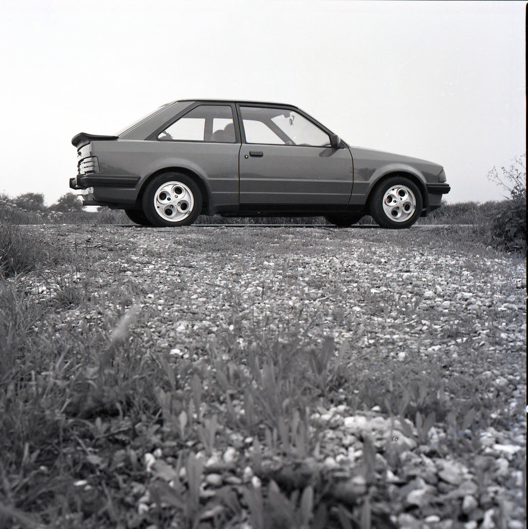 This archival image documents the 1985 Ford Escort Mark III XR3i low side view on scenic road and is preserved in the Ford Heritage Vault as part of Ford Motor Company's historic photographic archive. Free for personal, non-commercial use. Ford He...
