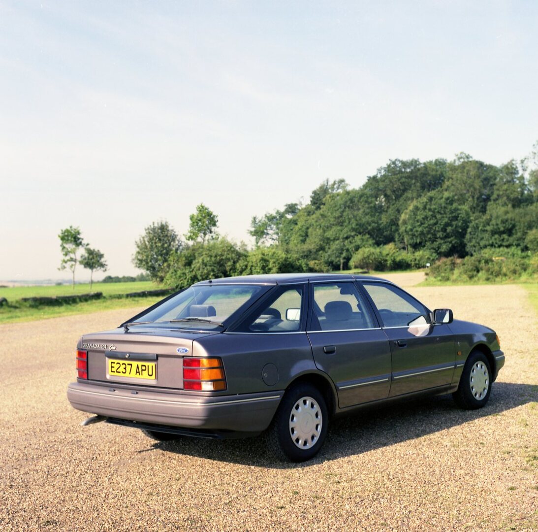 This archival image documents the 1987 Ford Granada Ghia 2.4i rear view on scenic road with trees and is preserved in the Ford Heritage Vault as part of Ford Motor Company's historic photographic archive. Free for personal, non-commercial use. For...