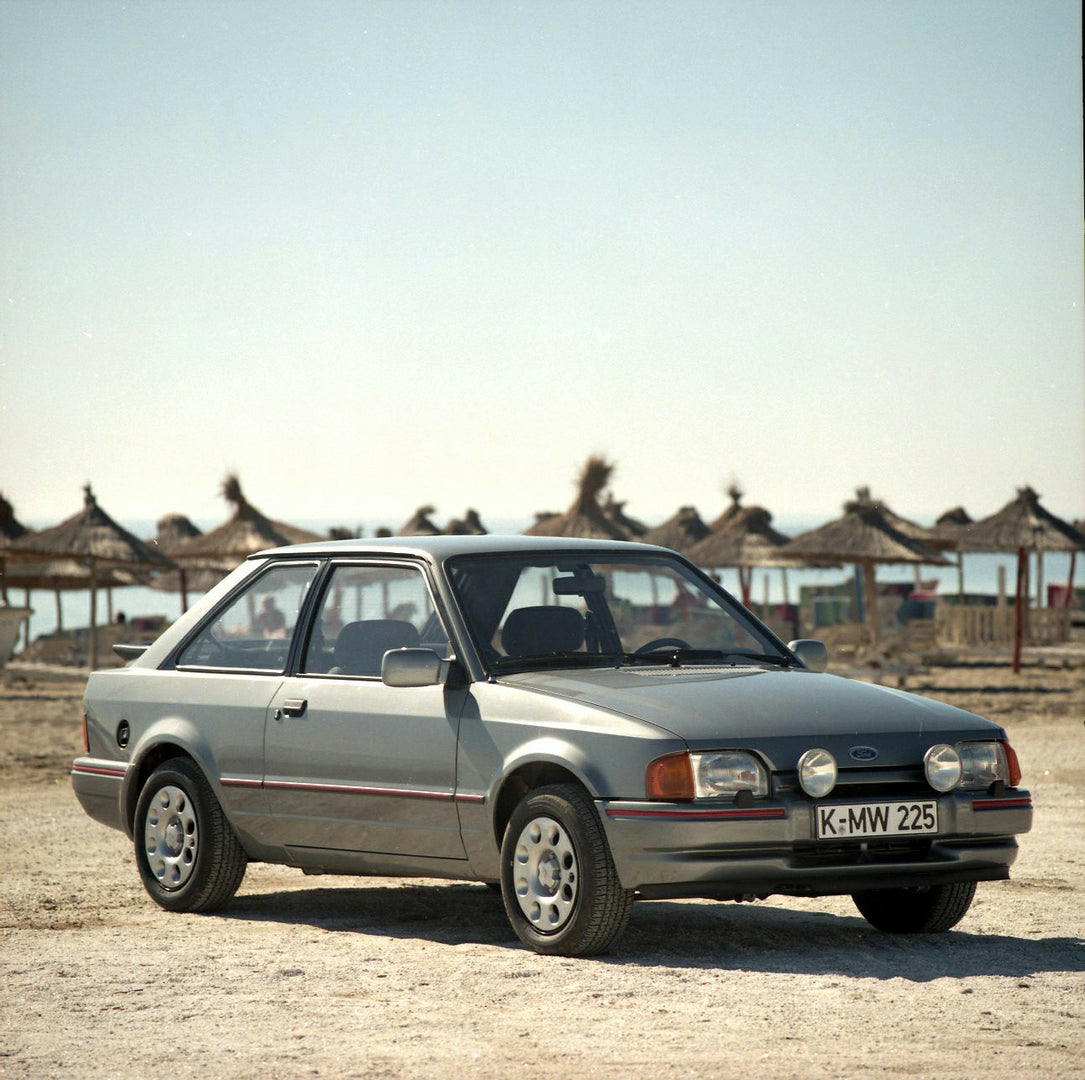 This archival image documents the 1985 Ford Escort Mark IV XR3i LHD on scenic beach with umbrellas and is preserved in the Ford Heritage Vault as part of Ford Motor Company's historic photographic archive. Free for personal, non-commercial use. Fo...