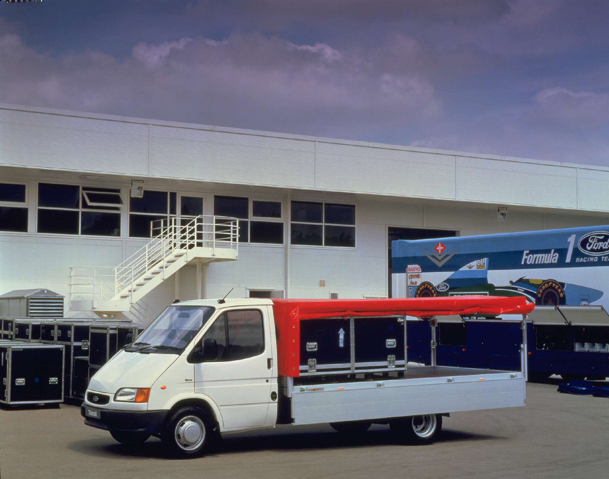 This archival image documents the 1996 Ford Transit Mark III Long Wheelbase Dropside behind building AR-2002-213709 and is preserved in the Ford Heritage Vault as part of Ford Motor Company's historic photographic archive. Free for personal, non-c...