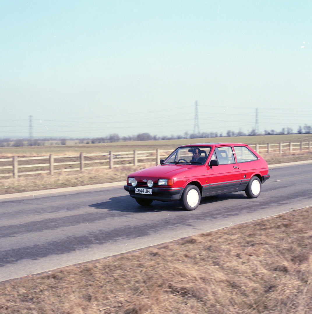 This archival image documents the 1986 Ford Fiesta Mark II 1.4 S action shot on scenic road with fence and trees and is preserved in the Ford Heritage Vault as part of Ford Motor Company's historic photographic archive. Free for personal, non-comm...