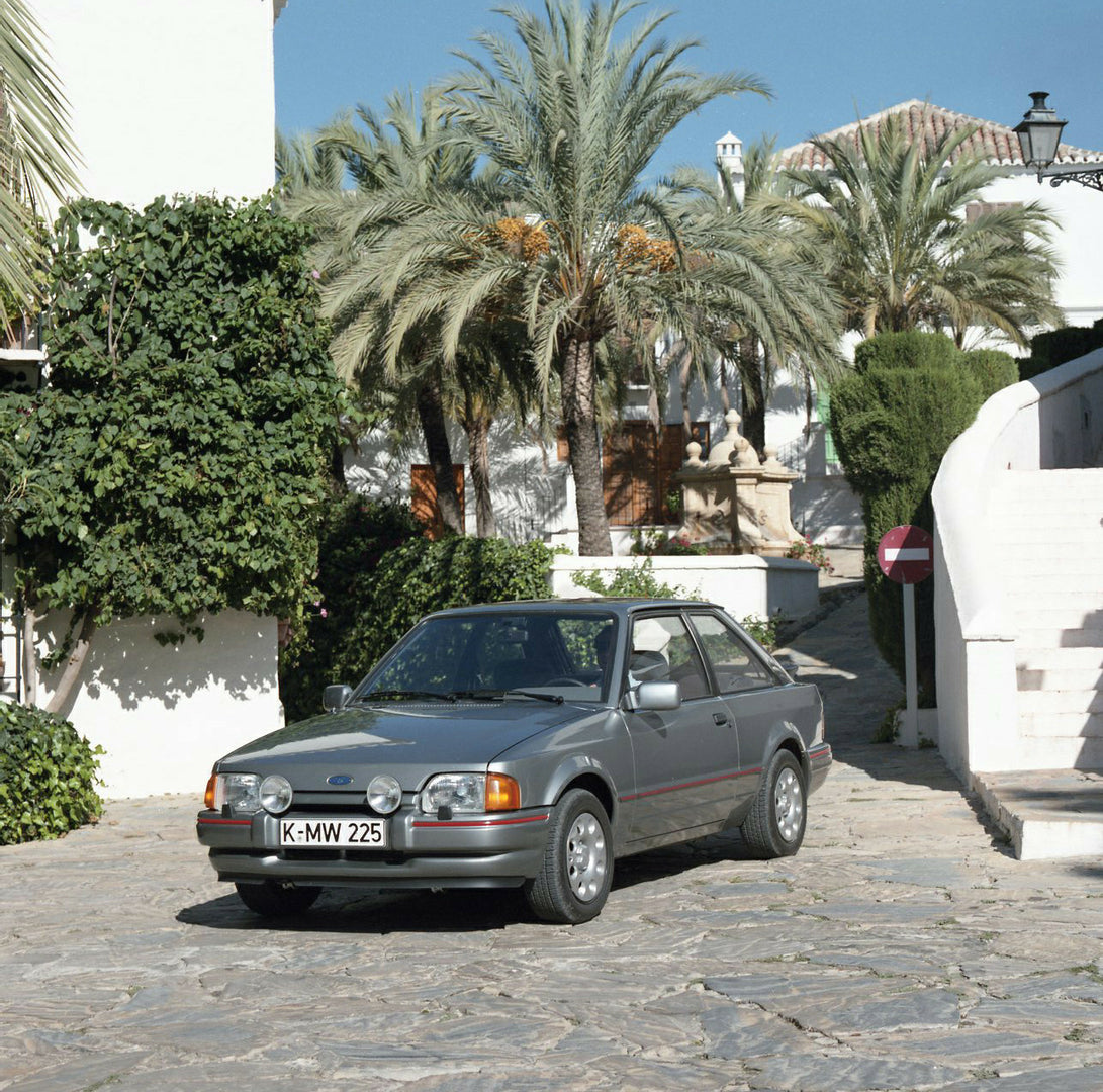 This archival image documents the 1985 Ford Escort Mark IV XR3i LHD with scenic palm trees and is preserved in the Ford Heritage Vault as part of Ford Motor Company's historic photographic archive. Free for personal, non-commercial use. Ford Herit...