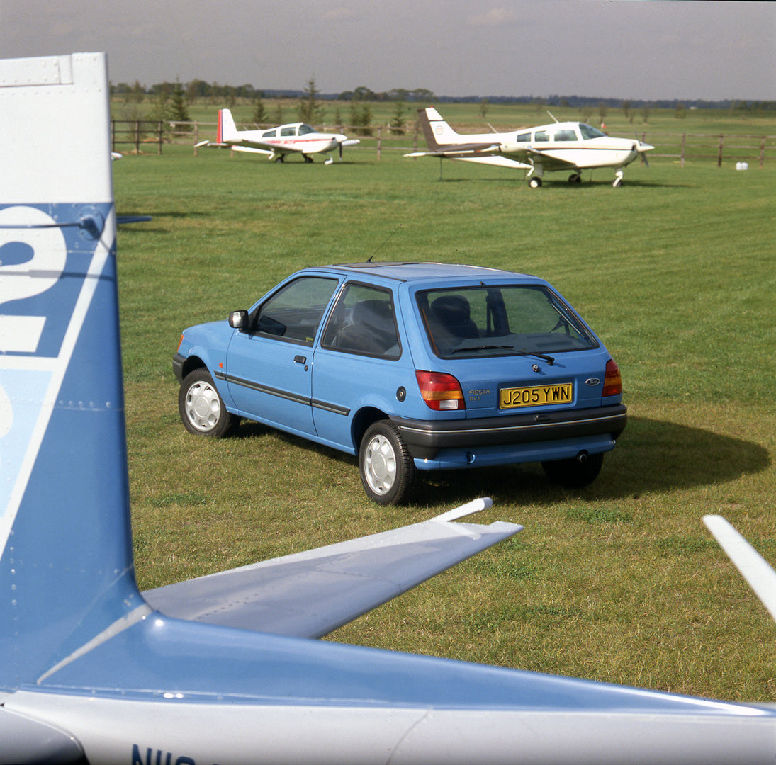 This archival image documents the 1991 Ford Fiesta Mark III 1.1 LX rear view in field with planes and is preserved in the Ford Heritage Vault as part of Ford Motor Company's historic photographic archive. Free for personal, non-commercial use. For...