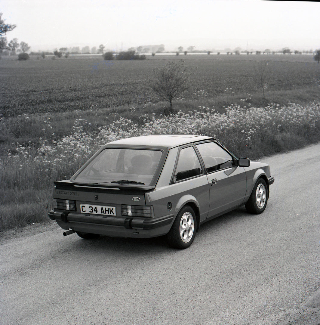 This archival image documents the 1985 Ford Escort Mark III XR3i rear view on scenic road and is preserved in the Ford Heritage Vault as part of Ford Motor Company's historic photographic archive. Free for personal, non-commercial use. Ford Herita...