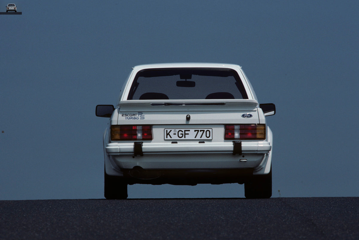 This archival image documents the 1984 Ford Escort Mark III RS Turbo rear view with scenic blue sky and is preserved in the Ford Heritage Vault as part of Ford Motor Company's historic photographic archive. Free for personal, non-commercial use. F...